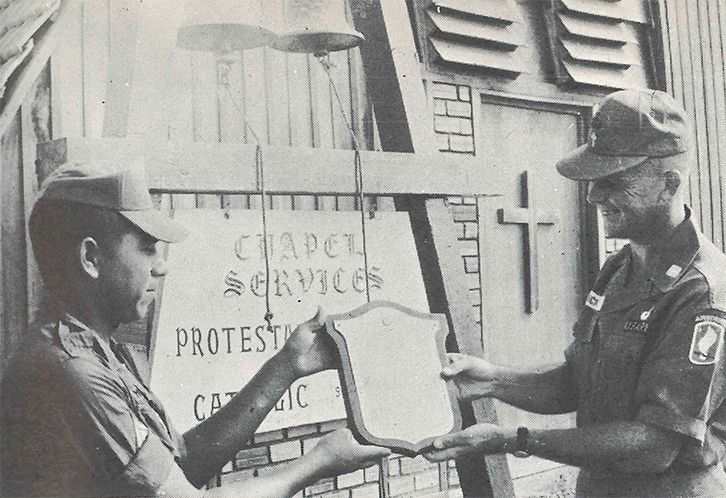 A hard-working leader, Chaplain Crick, and a young soldier examine the plaque they will place on the chapel they built in honor of their fallen comrades.