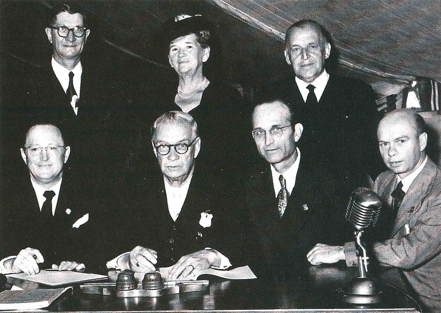 Seated at the table are signers of the amalgamation agreement: J. H. Walker Sr.; F. J. M. Beetge, moderator of the Full Gospel Church; H. L. Chesser; and H. R. Carter, secretary general of the Full Gospel Church. Witnessing the ceremony are J. H. Saayman, Mrs. Saayman, and A. H. Cooper